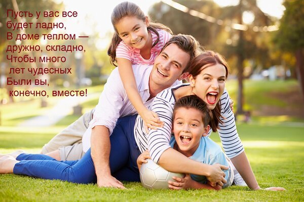 Счастливая семья смеется на траве в парке. Теплое фото с пожеланием семейного благополучия, гармонии и единства. Идеально для тем о семье и счастье. Открытка Пусть у вас все будет ладно, в доме теплом — дружно, складно, чтобы много лет чудесных были вы... Счастливая семья из четырех человек — папа, мама, сын и дочь — весело проводят время на зеленой лужайке в парке. На фото запечатлен момент искренней радости, смеха и крепких семейных уз. На фоне расположено трогательное пожелание на русском языке о гармонии, тепле и единстве в доме