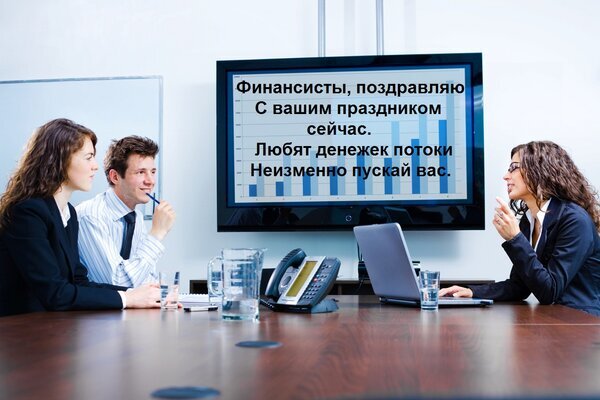 Поздравительная картинка для финансистов с текстом и рабочим графиком. Идеально для поздравления с профессиональным праздником в финансовой сфере. Открытка Финансисты, поздравляю С вашим праздником сейчас. Любят денежек потоки Неизменно пускай вас. Изображение представляет собой поздравительную открытку для финансистов. На фото запечатлена рабочая обстановка в офисе: группа людей (мужчина и две женщины) сидит за столом переговоров с ноутбуками и документами. На заднем плане на большом экране телевизора отображен график и текст поздравительного стихотворения на русском языке: «Финансисты, поздравляю с вашим праздником сейчас. Любят денежек потоки неизменно пускай вас»