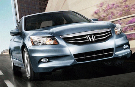 Стильный светло-голубой седан Honda в динамике. Крупный план передней части: решетка радиатора, фары и аэродинамичный дизайн кузова. Открытка Автомобиль Хонда Аккорд 2012 На изображении представлен стильный современный седан Honda в светло-голубом (серебристом) цвете. Автомобиль запечатлен в динамике на городской улице, что подчеркивает его аэродинамичный дизайн, обтекаемые формы кузова и спортивный характер. Крупным планом видны детали передней части: фирменная хромированная решетка радиатора с логотипом Honda, выразительные фары головного света и противотуманные фары в бампере. Кадр выполнен под углом, акцентируя внимание на колесах, текстуре кузова и игре света на металлике