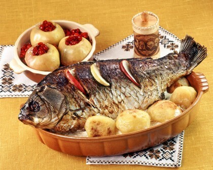 Запеченная рыба с золотистым картофелем и фаршированными яблоками. Аппетитное домашнее блюдо для праздничного обеда или семейного ужина. Открытка Рыба рыба еда Аппетитное блюдо из запеченной рыбы с картофелем и начинкой из яблок. На фотографии представлен цельный запеченный карп или другая крупная рыба в керамической форме, окруженная золотистым молодым картофелем. Рядом подаются десертные яблоки, фаршированные ягодами. Изображение передает атмосферу домашнего уюта и праздничного застолья в традиционном стиле