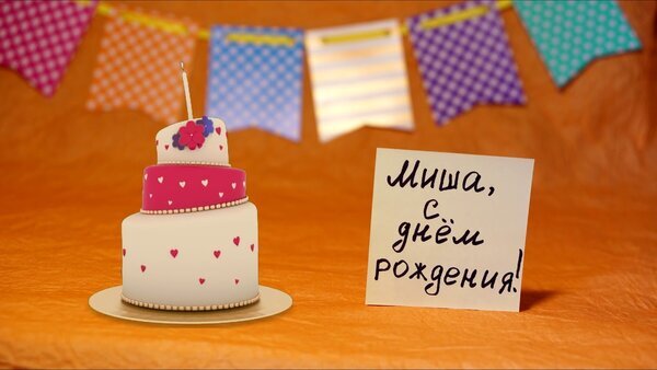 Праздничный торт с сердечками и поздравительная открытка «Миша, с днем рождения!» на фоне разноцветных флажков. Идеально для темы дня рождения. Открытка С днем рождения Миша! Праздничная композиция с двухъярусным тортом, украшенным розовыми сердечками и цветами, на фоне ярких разноцветных флажков. Рядом с тортом расположена белая карточка с рукописной надписью на русском языке «Миша, с днем рождения!»