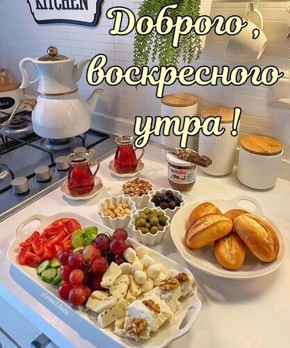 Аппетитный завтрак на кухне с надписью «Доброго воскресного утра!». Свежая выпечка, сыр, фрукты и чай для уютного начала дня. Открытка Доброго, воскресного утра! Уютный завтрак на светлой кухне с надписью «Доброго воскресного утра!». На столе накрыт аппетитный стол: свежие круассаны, сыр, виноград, томаты, оливки, орехи и ягоды. Рядом стоит чайник, чашка чая и баночка Нутеллы