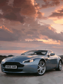 Спортивный автомобиль Aston Martin на фоне живописного заката. Эстетичное фото премиального купе в мягком вечернем свете. Анимированная открытка Автомобиль имя маргарита Эстетичный снимок спортивного автомобиля Aston Martin в мягком свете заката. Серебристый кузов люксового купе эффектно контрастирует с драматичным небом, окрашенным в розовые и золотистые тона. Композиция подчеркивает обтекаемые линии дизайна, премиальный стиль и динамику автомобиля на фоне живописного вечернего пейзажа