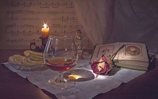 Романтический натюрморт: бокал вина, горящая свеча, старинная книга и роза на фоне нот. Атмосферное фото в винтажном стиле для эстетичного оформления. Открытка Фотоальбом бокал роза свеча лимон Атмосферная натюрмортная композиция в винтажном стиле, создающая романтическое и меланхоличное настроение. На столе, освещенном мягким светом горящей свечи, стоит бокал красного вина, рядом лежит раскрытая старинная книга с портретами, нежная роза и тарелка с дольками лимона. Фон украшен нотной грамотой, что добавляет эстетику классической музыки и уюта