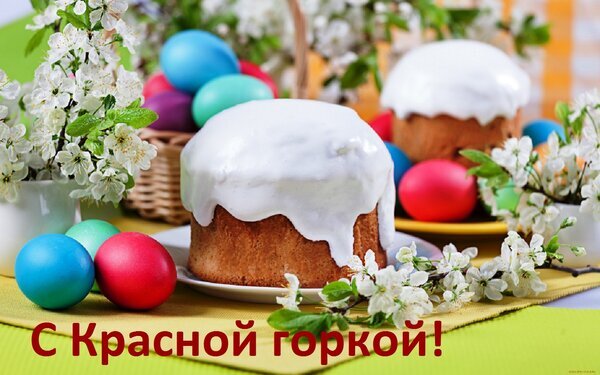 Праздничное фото к Красной горке: пасхальный кулич в глазури, крашеные яйца и цветущие ветки белых деревьев. Поздравление с весенним праздником! Открытка С Красной горкой! Красочное праздничное изображение, посвященное празднику Красной горки. На переднем плане расположен традиционный пасхальный кулич, обильно политый белой глазурью, стоящий на белой тарелке. Вокруг кулича разложены разноцветные крашеные яйца (синие, красные, бирюзовые) и расставлены вазы с цветущими ветками белой вишни или яблони. Композиция дополнена яркой желтой и зеленой скатертью, создающей весеннее настроение. В нижней части изображения расположена праздничная надпись на русском языке: С Красной горкой!