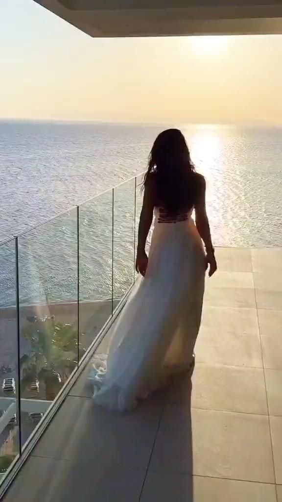 Открытка с пожеланиями Хорошего Отпуска. Доброе утро 🌹🕊️Good morning a woman in a white dress is looking out at the ocean from a balcony with glass railings