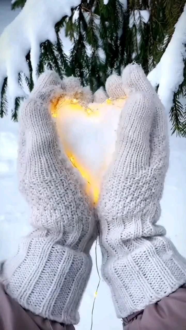 Открытка на Зиму. two hands in mittens hold a heart shaped light up on the snow covered ground