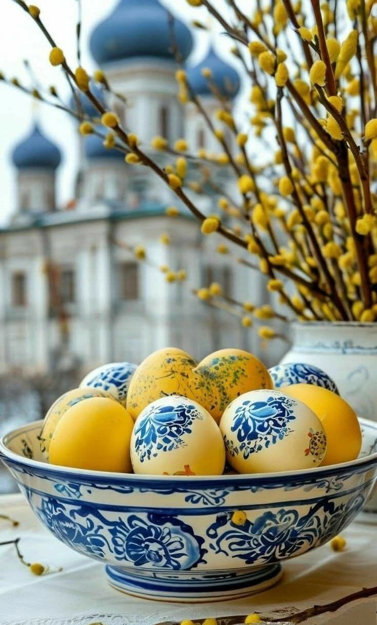 Открытка на Пасху. some yellow eggs in a blue and white bowl on a table next to a vase with flowers